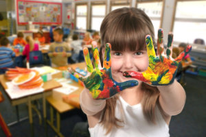 young school age child painting with her hands in class