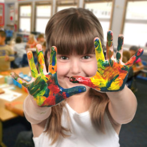 young school age child painting with her hands in class